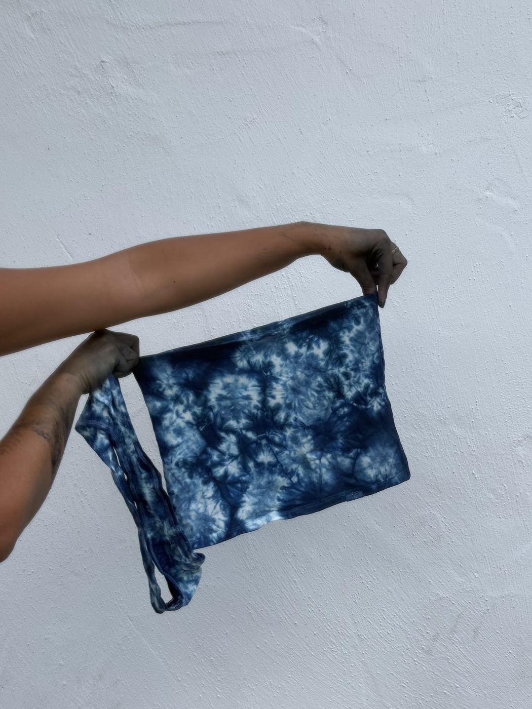 Hands holding a shibori-dyed indigo tube top against a white wall