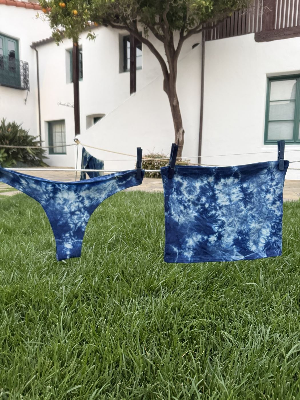 Indigo-dyed undergarment and tube top clipped to a line over green grass