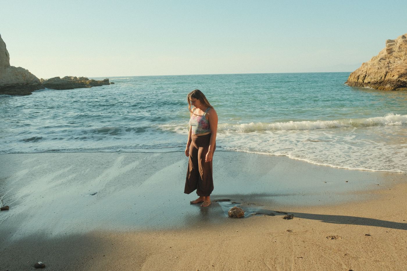 A person in a plant-dyed tank standing at the edge of the surf