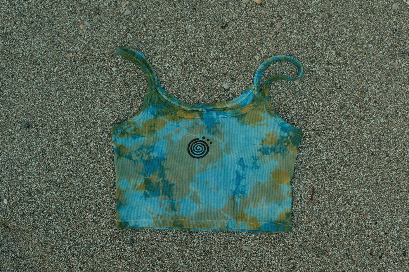 A blue and gold plant-dyed tank laid on wet sand
