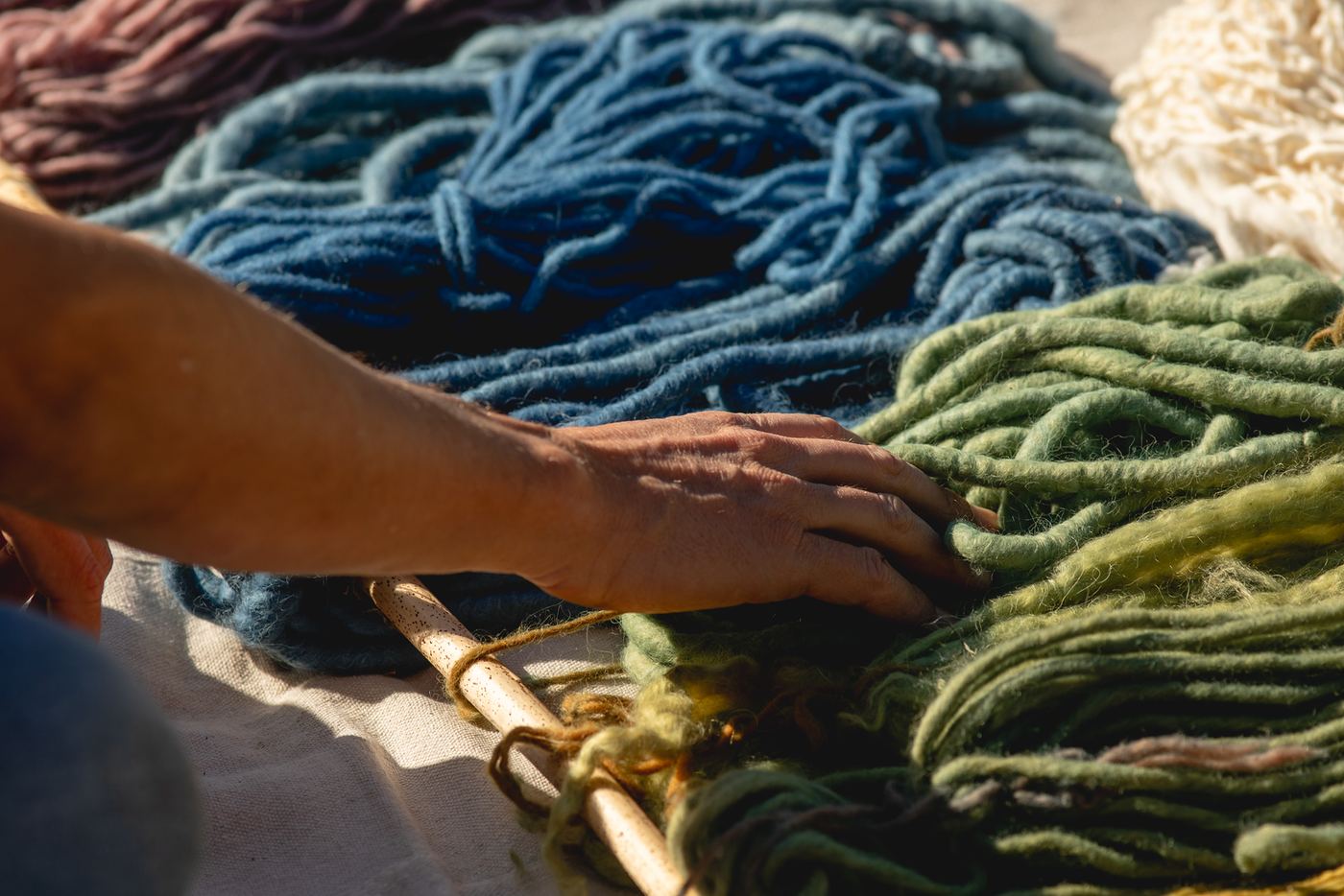 A hand resting on piles of plant-dyed wool in blue and green