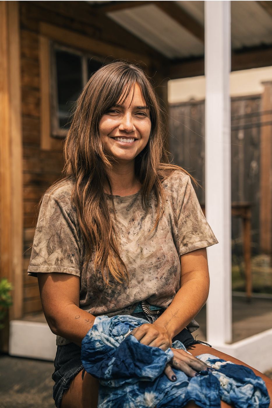 Felise seated outside, smiling, indigo-dyed cloth in her lap